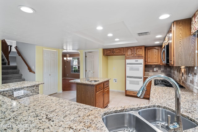 kitchen with sink, light stone countertops, light hardwood / wood-style floors, double oven, and backsplash