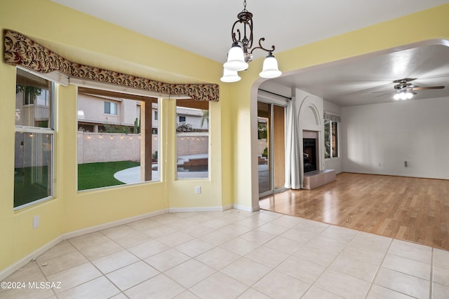 tiled empty room featuring ceiling fan with notable chandelier