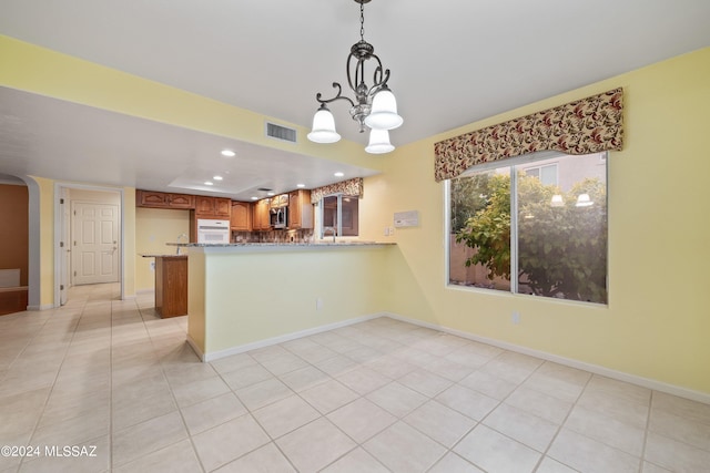 kitchen with a chandelier, kitchen peninsula, pendant lighting, oven, and light tile patterned floors