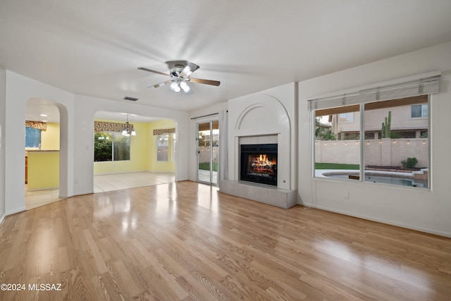 unfurnished living room featuring ceiling fan with notable chandelier, light wood-type flooring, and plenty of natural light