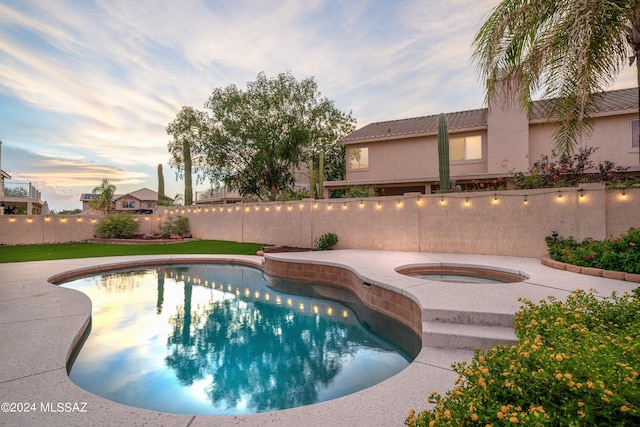 pool at dusk featuring an in ground hot tub