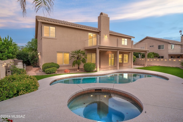 pool at dusk featuring a patio and an in ground hot tub