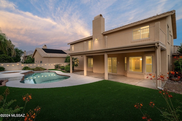 pool at dusk with an in ground hot tub, a patio, and a yard