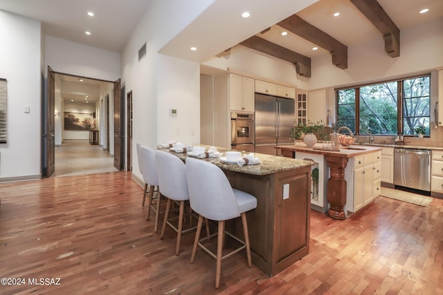 kitchen featuring a high ceiling, stainless steel appliances, a center island, light stone counters, and beam ceiling