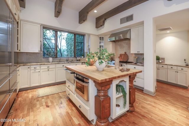 kitchen featuring wooden counters, a center island, wall chimney exhaust hood, and white cabinetry