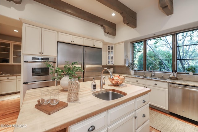 kitchen with stainless steel appliances, white cabinetry, beamed ceiling, and sink