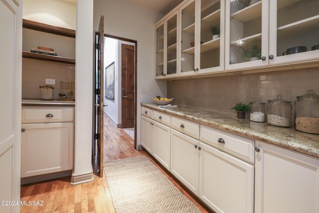 bar featuring backsplash, white cabinets, light hardwood / wood-style floors, and light stone countertops