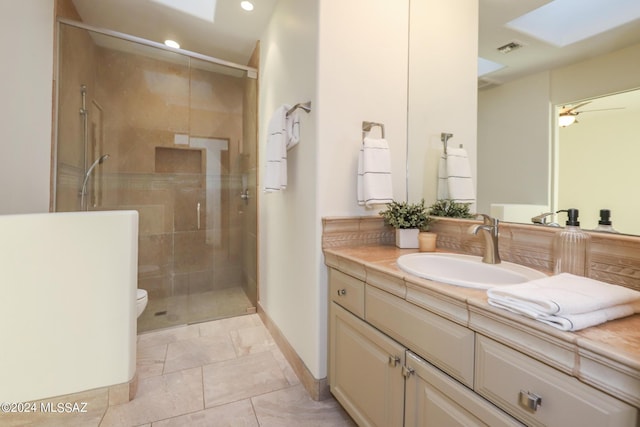 bathroom with toilet, a skylight, ceiling fan, a shower with shower door, and vanity