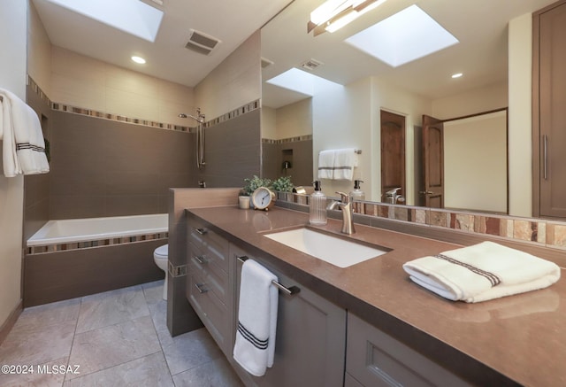 full bathroom with tile patterned flooring, toilet, a skylight, vanity, and tiled shower / bath