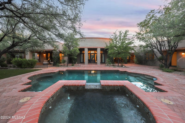 pool at dusk featuring a patio and an in ground hot tub