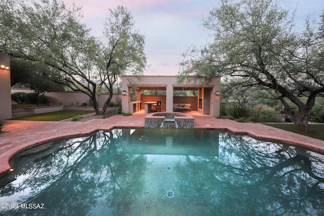 pool at dusk featuring exterior bar, a patio, and an in ground hot tub