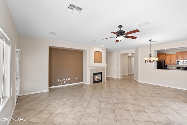 unfurnished living room with ceiling fan with notable chandelier, light tile patterned floors, and a tile fireplace