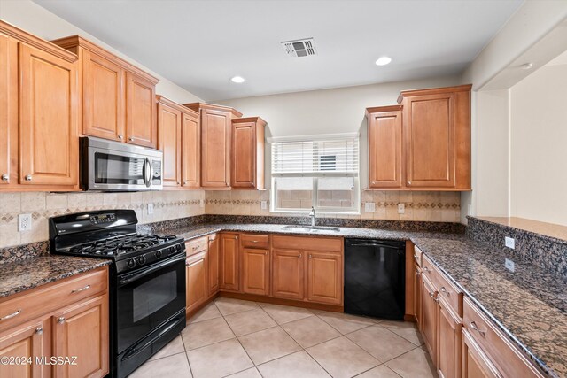 kitchen featuring dark stone countertops, tasteful backsplash, light tile patterned floors, black appliances, and sink