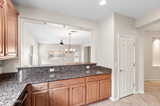 kitchen featuring kitchen peninsula, ceiling fan with notable chandelier, dark stone counters, and light tile patterned flooring