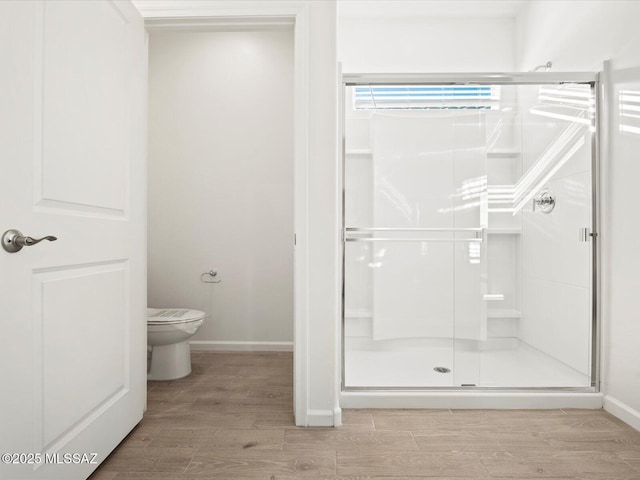 bathroom featuring a stall shower, baseboards, toilet, and wood finished floors