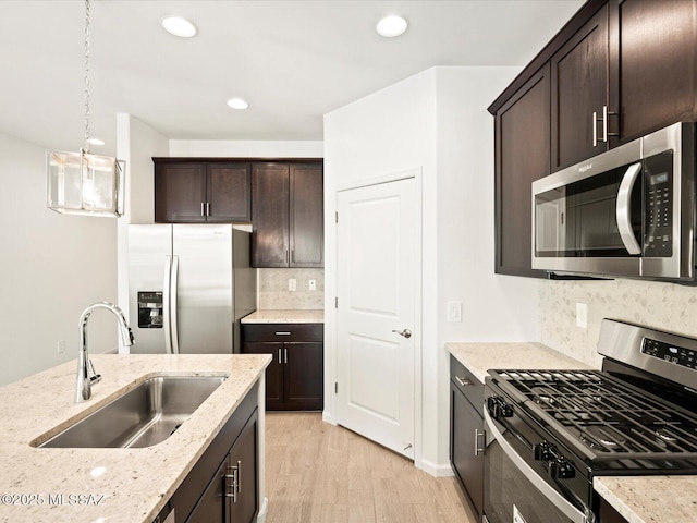 kitchen with light stone countertops, dark brown cabinetry, appliances with stainless steel finishes, light wood-style floors, and a sink