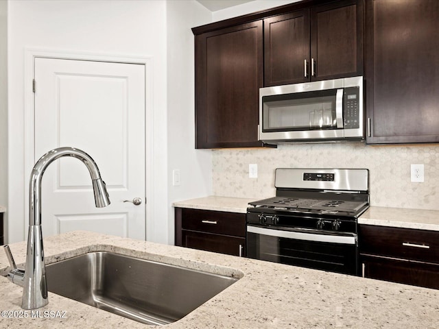 kitchen with a sink, light stone counters, tasteful backsplash, stainless steel appliances, and dark brown cabinets