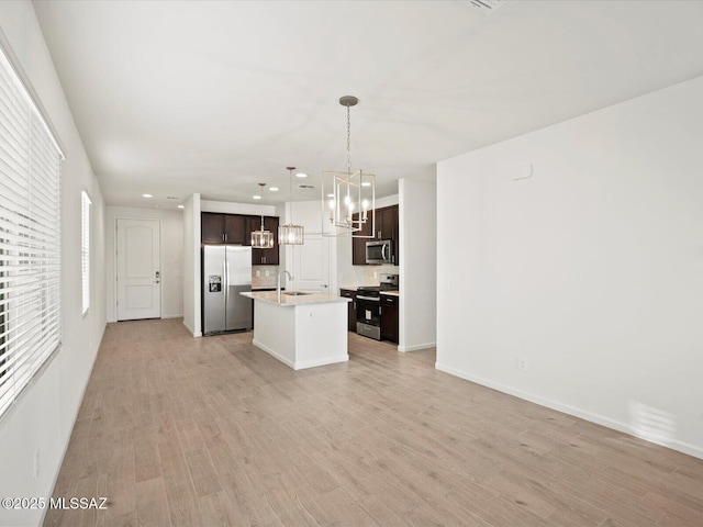 kitchen with an inviting chandelier, a sink, stainless steel appliances, dark brown cabinetry, and light wood-type flooring