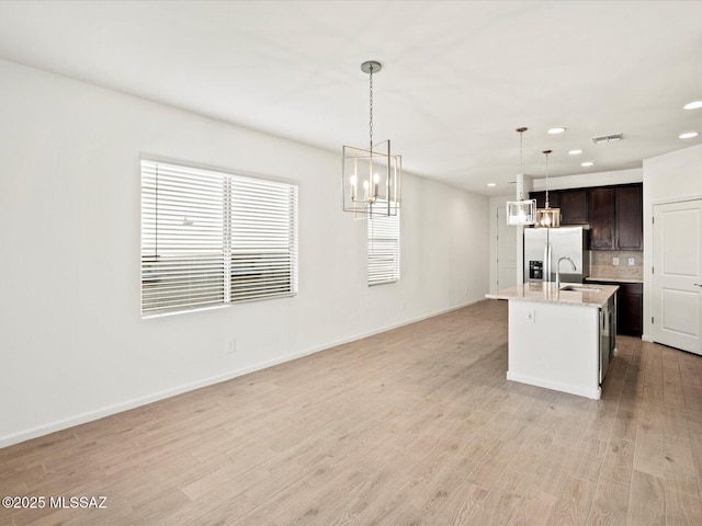 kitchen with decorative light fixtures, stainless steel refrigerator with ice dispenser, tasteful backsplash, dark brown cabinetry, and light wood-type flooring