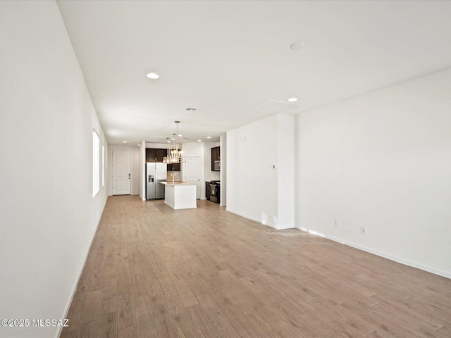 unfurnished living room featuring baseboards, recessed lighting, light wood-type flooring, and a chandelier