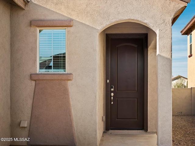 property entrance featuring stucco siding and fence