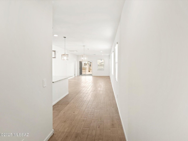 hall featuring baseboards, a notable chandelier, and wood finished floors