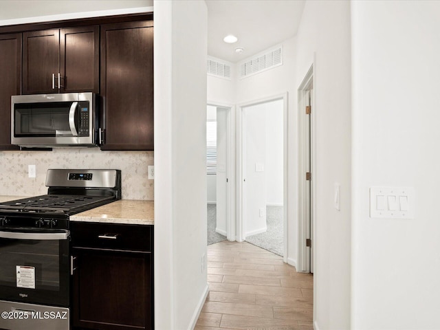 kitchen with light wood-type flooring, visible vents, dark brown cabinetry, appliances with stainless steel finishes, and decorative backsplash