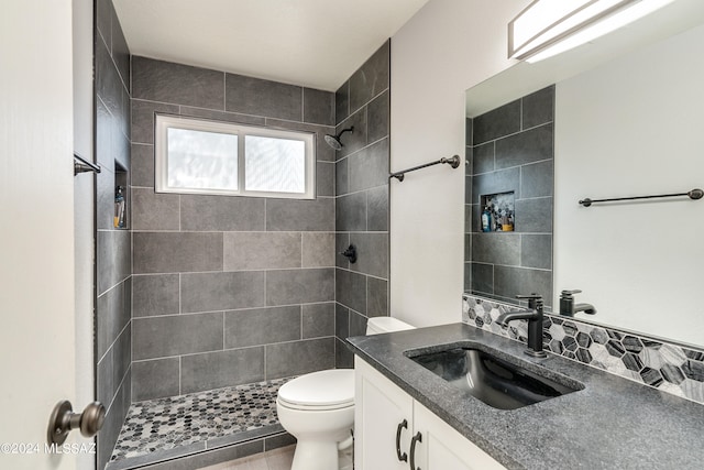 bathroom featuring toilet, vanity, a tile shower, and tile patterned flooring