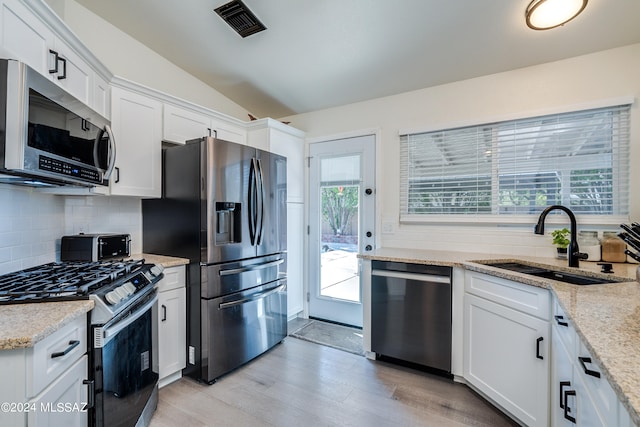 kitchen featuring stainless steel appliances, vaulted ceiling, white cabinets, light stone counters, and sink