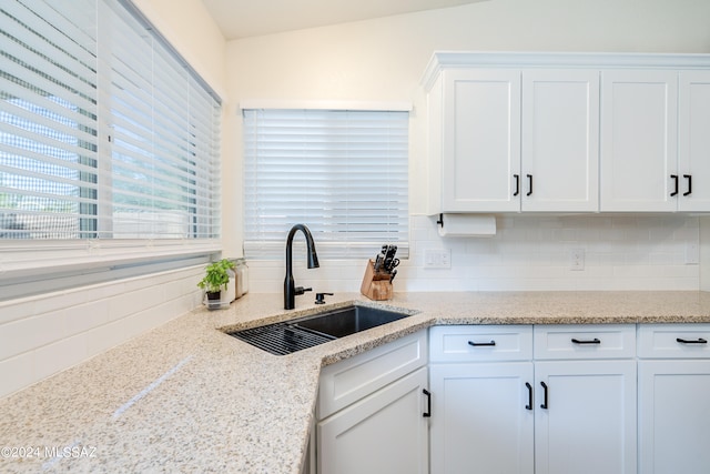 kitchen featuring tasteful backsplash, white cabinets, sink, and light stone counters