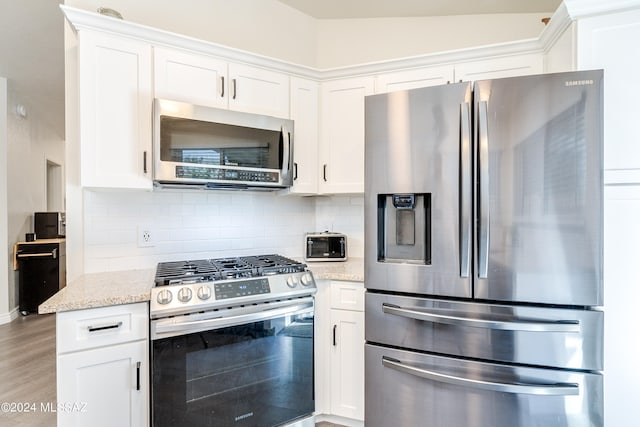 kitchen with vaulted ceiling, appliances with stainless steel finishes, white cabinets, and light stone countertops