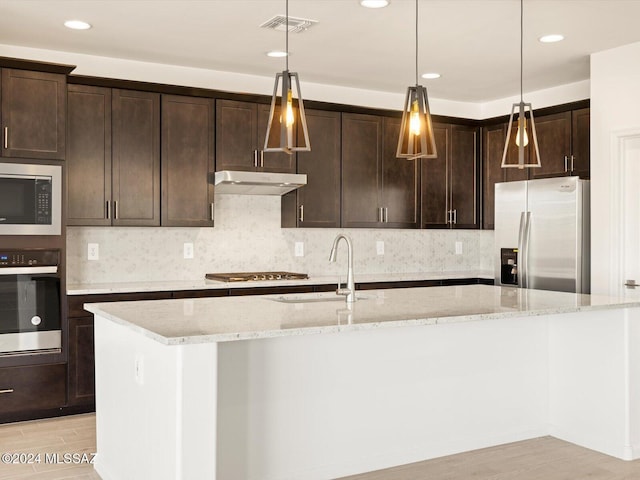 kitchen with appliances with stainless steel finishes, sink, light stone counters, and dark brown cabinets