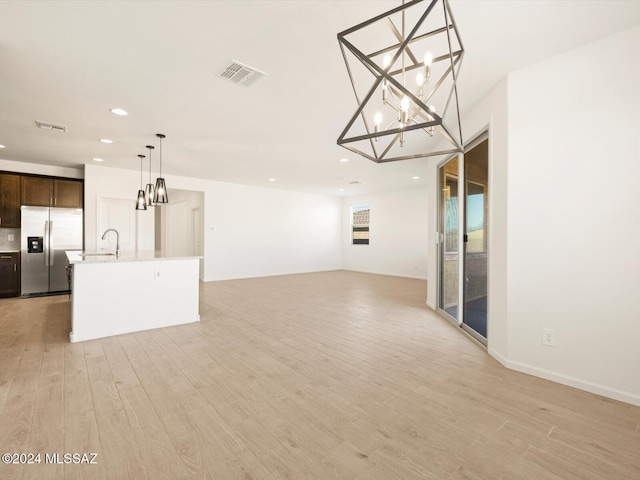 unfurnished living room featuring sink, a notable chandelier, and light wood-type flooring