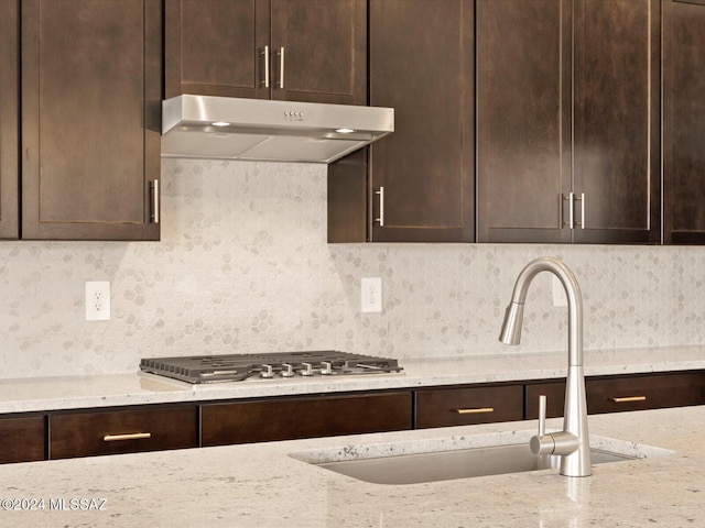 kitchen with tasteful backsplash, sink, dark brown cabinets, and light stone countertops