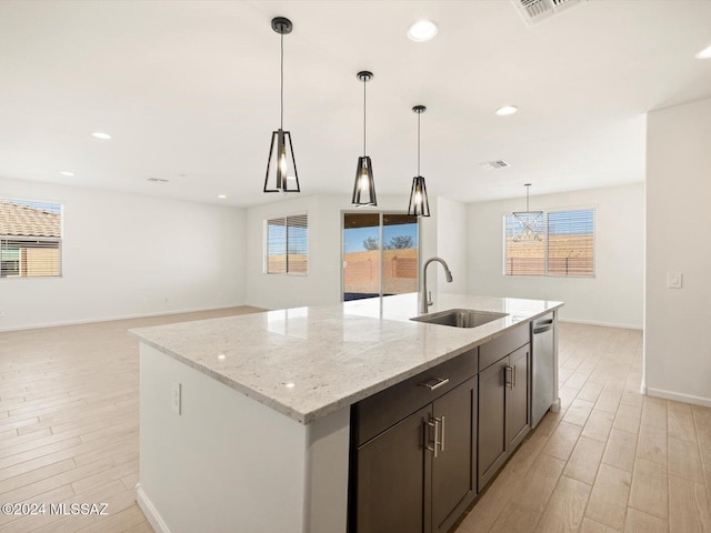 kitchen featuring sink, hanging light fixtures, light hardwood / wood-style flooring, an island with sink, and light stone countertops