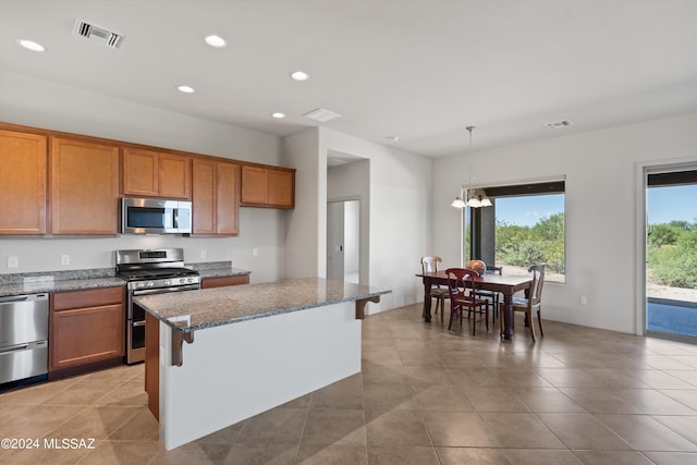 kitchen with hanging light fixtures, dark stone countertops, a breakfast bar, a kitchen island, and appliances with stainless steel finishes