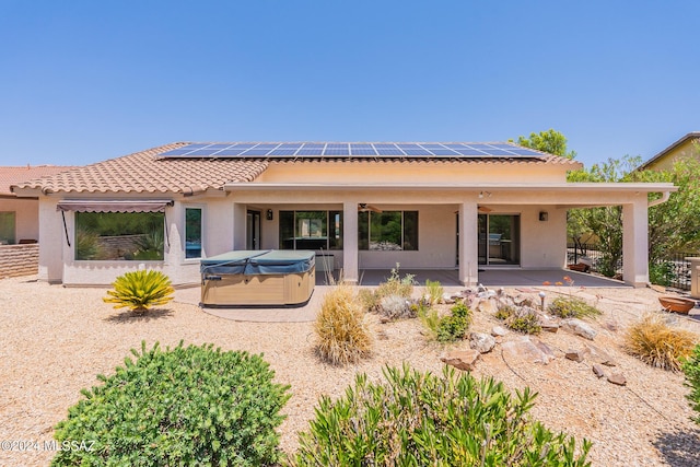 back of property with a patio area, a hot tub, and solar panels