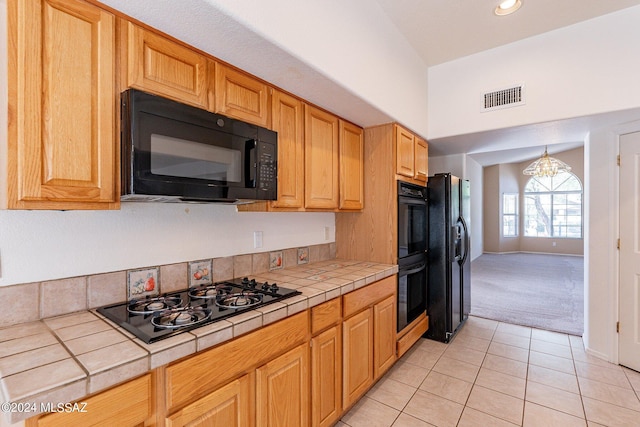 kitchen featuring an inviting chandelier, tile countertops, light carpet, and black appliances