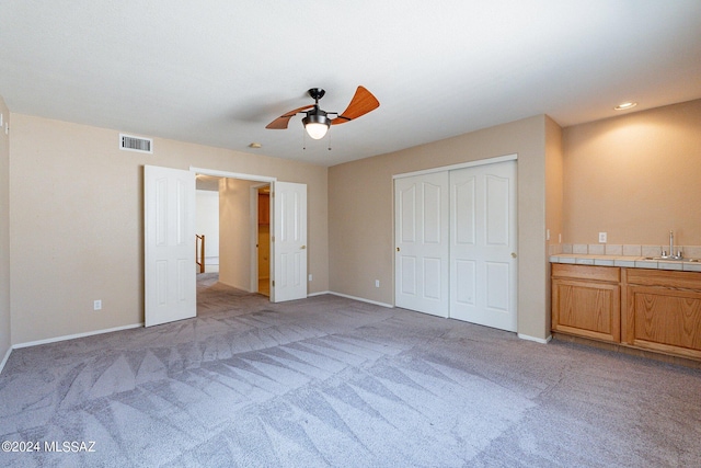 unfurnished bedroom with sink, light colored carpet, a closet, and ceiling fan