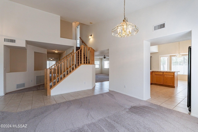 carpeted empty room with ceiling fan with notable chandelier and a high ceiling