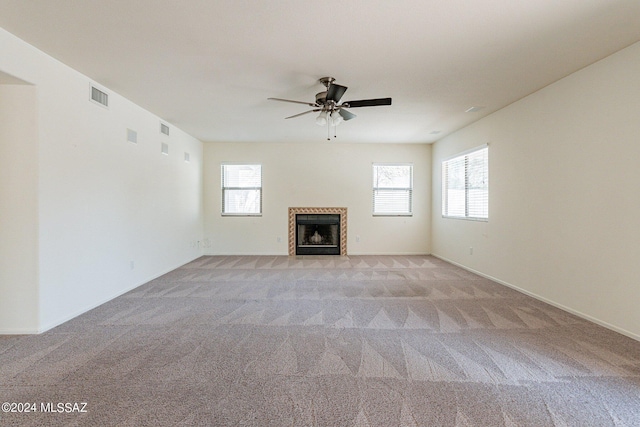 unfurnished living room with a tiled fireplace, a healthy amount of sunlight, and light colored carpet