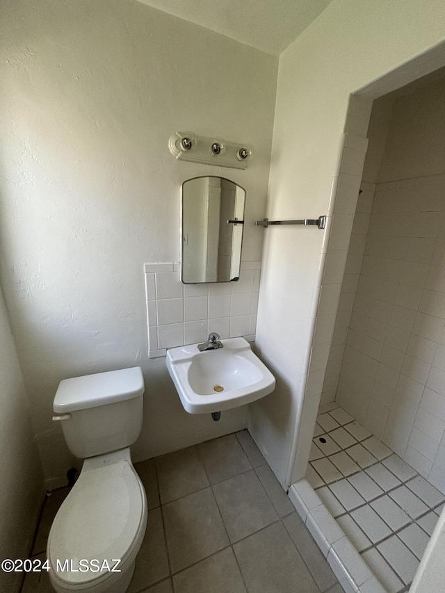 bathroom with sink, tile walls, tile patterned flooring, tiled shower, and toilet