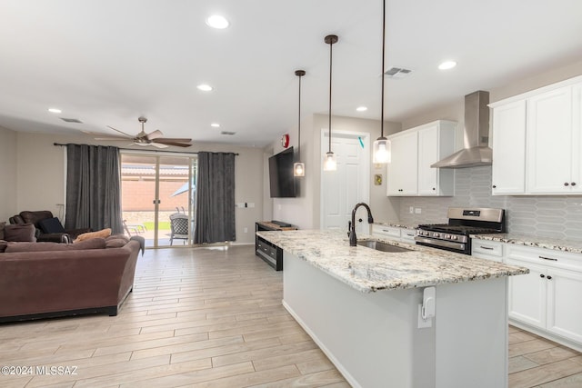 kitchen with sink, white cabinets, hanging light fixtures, stainless steel range with gas stovetop, and wall chimney exhaust hood