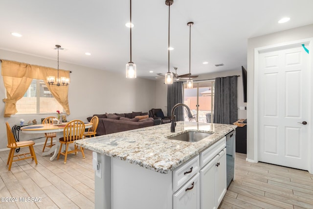 kitchen featuring sink, white cabinetry, hanging light fixtures, light stone counters, and a center island with sink