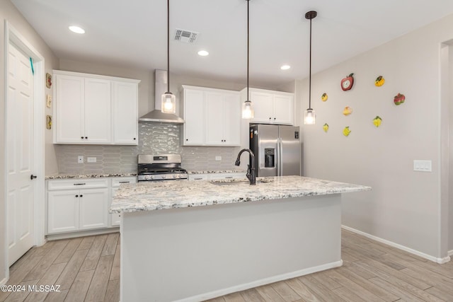 kitchen featuring a kitchen island with sink, wall chimney range hood, white cabinetry, and appliances with stainless steel finishes