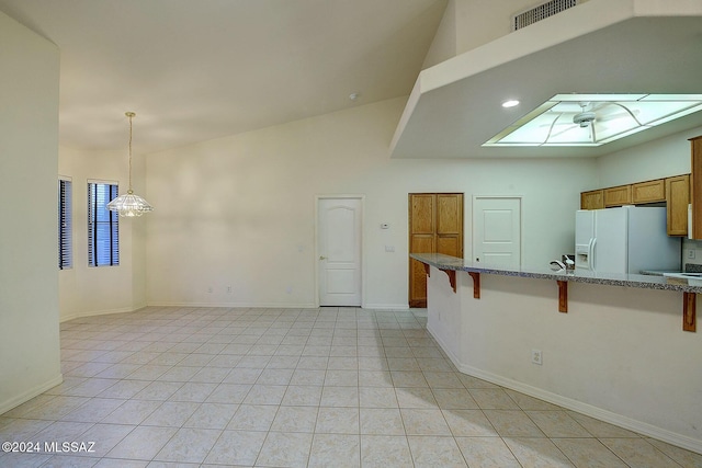 interior space with pendant lighting, a kitchen bar, white refrigerator with ice dispenser, and light tile patterned floors