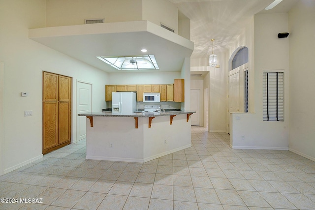 kitchen with light tile patterned floors, white appliances, a breakfast bar area, and a towering ceiling