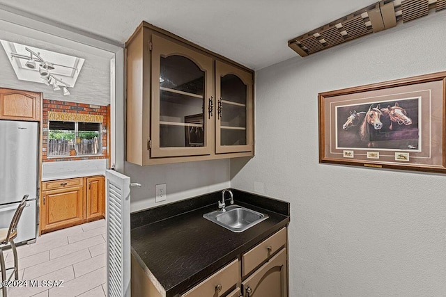 kitchen with glass insert cabinets, dark countertops, a sink, and freestanding refrigerator