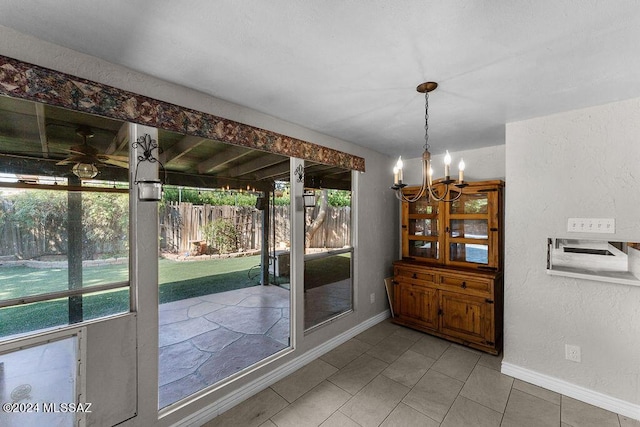 interior space featuring tile patterned floors, ceiling fan with notable chandelier, baseboards, and a textured wall