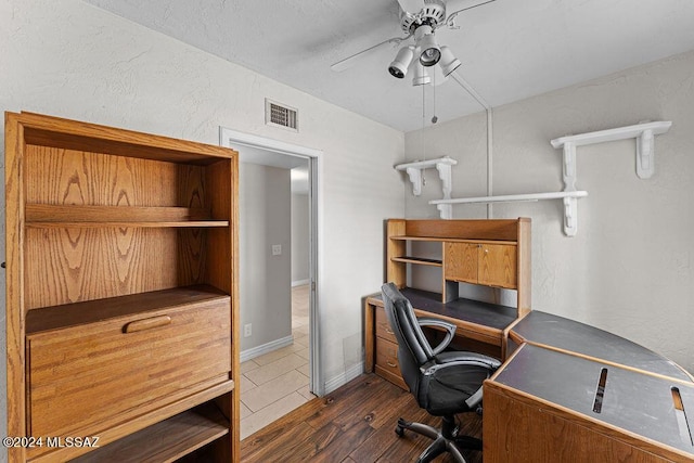 home office featuring ceiling fan, a textured wall, dark wood-type flooring, visible vents, and baseboards